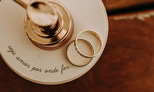 Mãos segurando alianças em cima de flores brancas